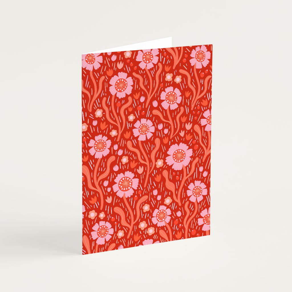 The Red Wildflowers Greetings Card stands upright, showcasing a red background with pink and orange dog roses and leaves inspired by the beauty of British wildflowers.