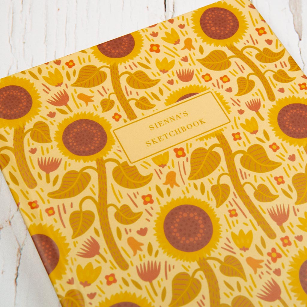 The Yellow Wildflowers Personalised Notebook features a yellow cover with British wildflowers, including sunflowers and foliage, plus a central box for your custom text.