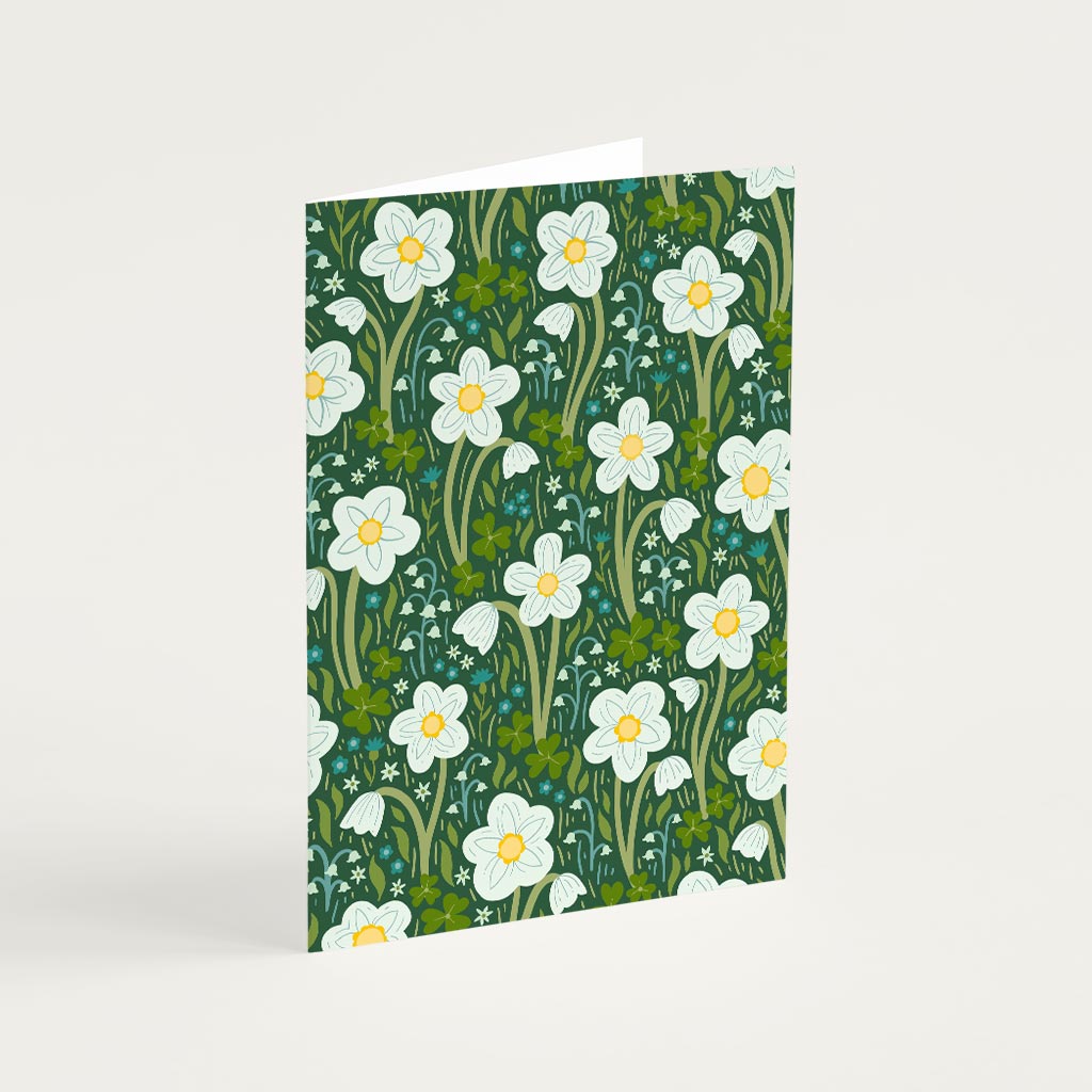 The Dark Green Wildflowers Greetings Card stands upright, showcasing British wildflowers such as wood anemones and lily of the valley with white petals and yellow centres on a dark green background.