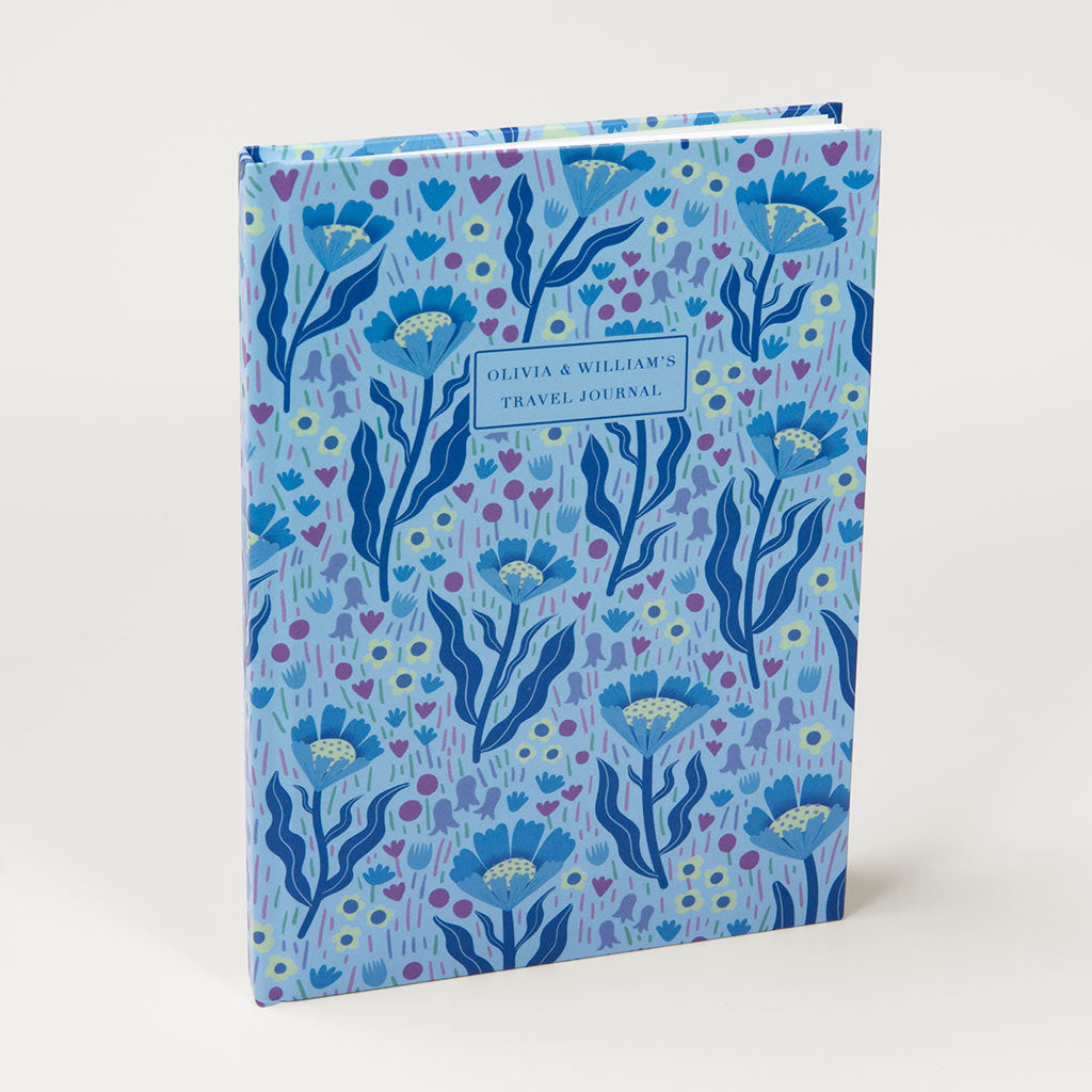 The Blue Wildflowers Personalised Notebook is a luxurious hardcover travel journal with a blue floral pattern inspired by British wildflowers and a custom text label section on the front cover.
