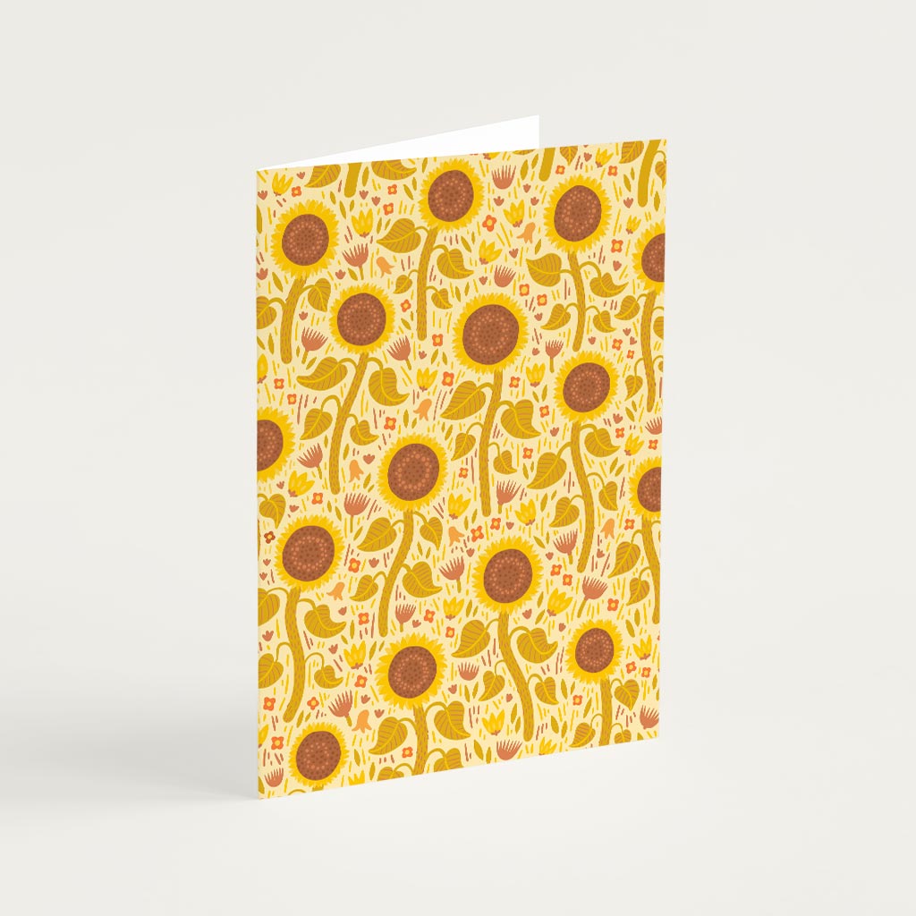 The Yellow Wildflowers Greetings Card stands upright and features a repeating pattern of sunflowers and yellow wildflowers on a light background.